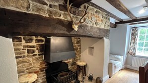 A stone fireplace with a black hearth, a wooden stool, a small table, and a kettle. - Ivy Cottage (Wareham)