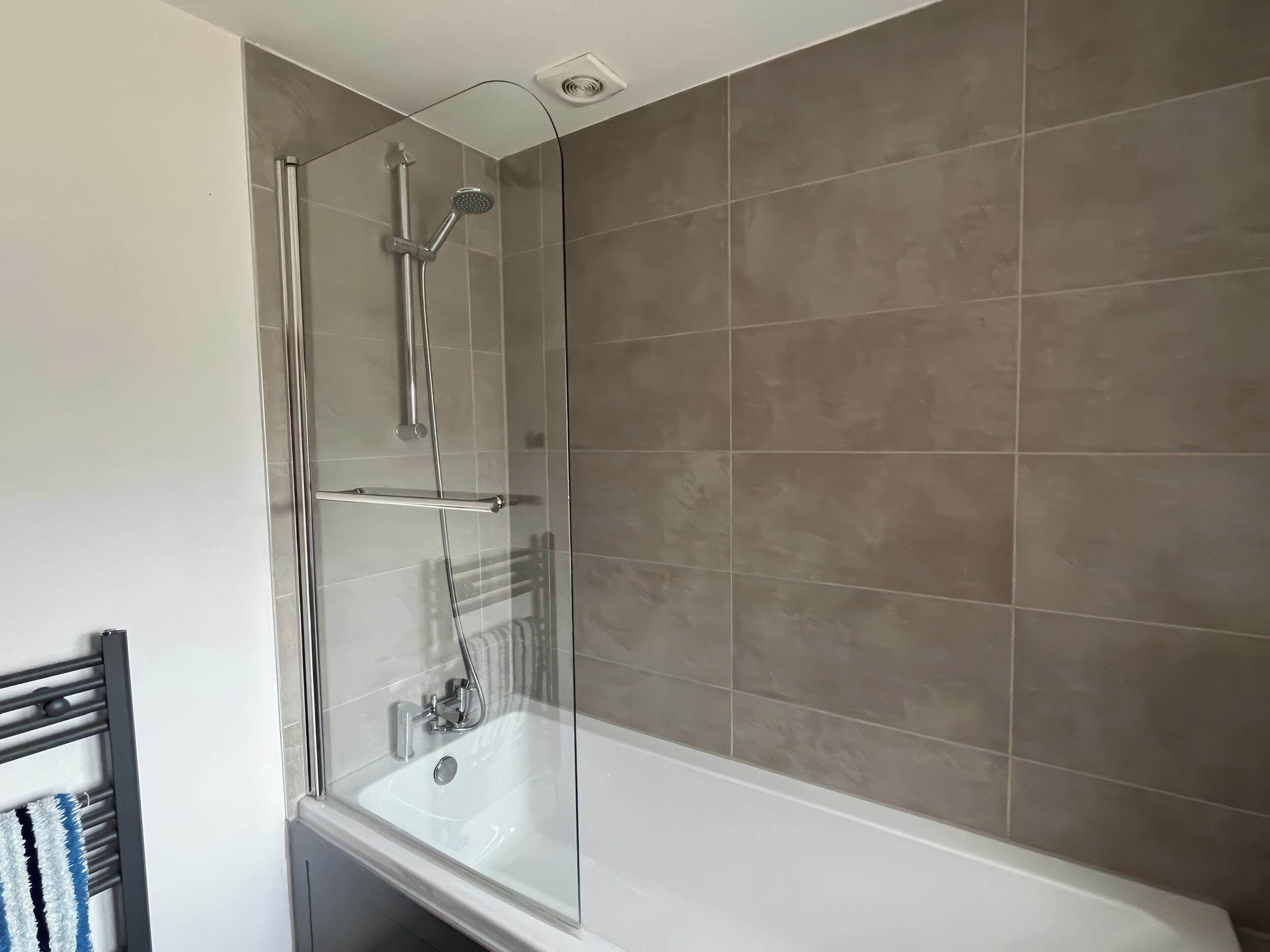 A modern bathroom with a glass-enclosed shower, a white bathtub, and beige tiles.