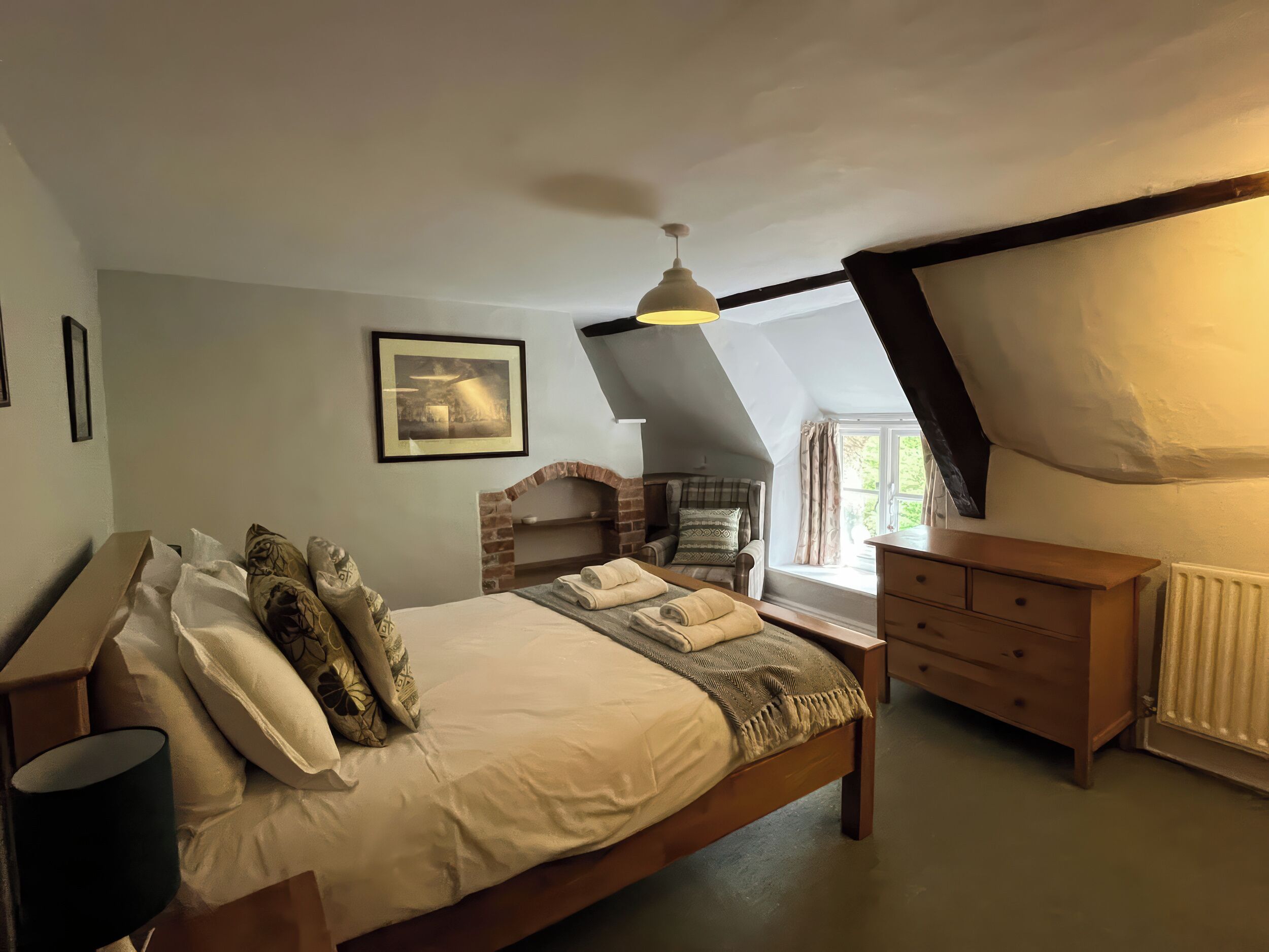 A bedroom with a bed, a chair, a dresser, a picture on the wall, and a window.