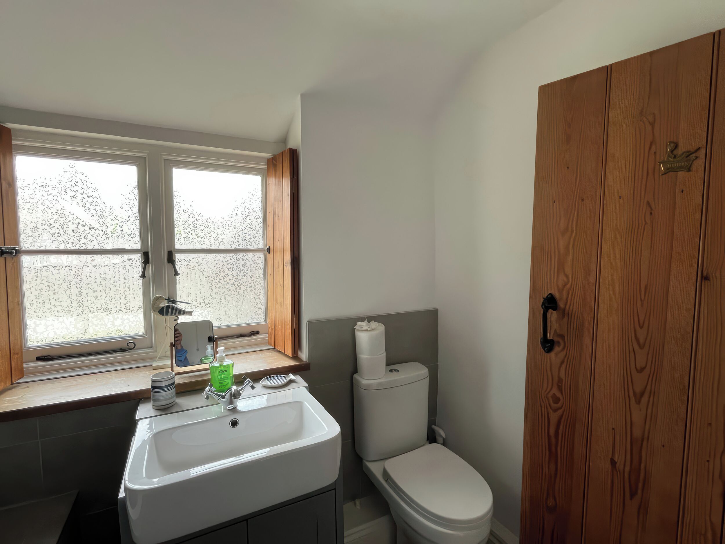 A bathroom with a window, a sink, a toilet, and wooden cabinets.