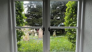 A window with a view of a cemetery, a statue, and a seashell decoration. - Ivy Cottage (Wareham)