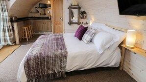 A cozy bedroom with a bed, a TV, and a kitchenette in the background. - Gelert Pod (Saint Asaph)
