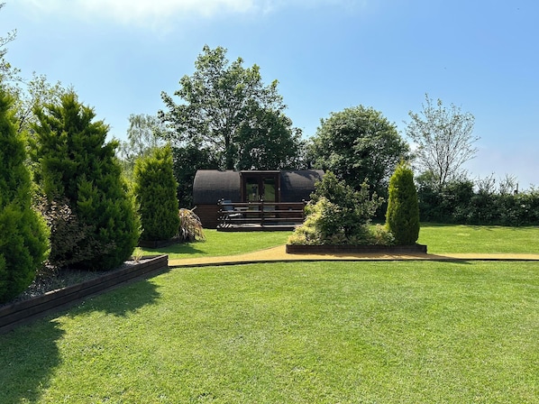 A well-maintained lawn with a small building featuring a door and windows, surrounded by various trees and shrubs. - Gelert Pod (Saint Asaph)