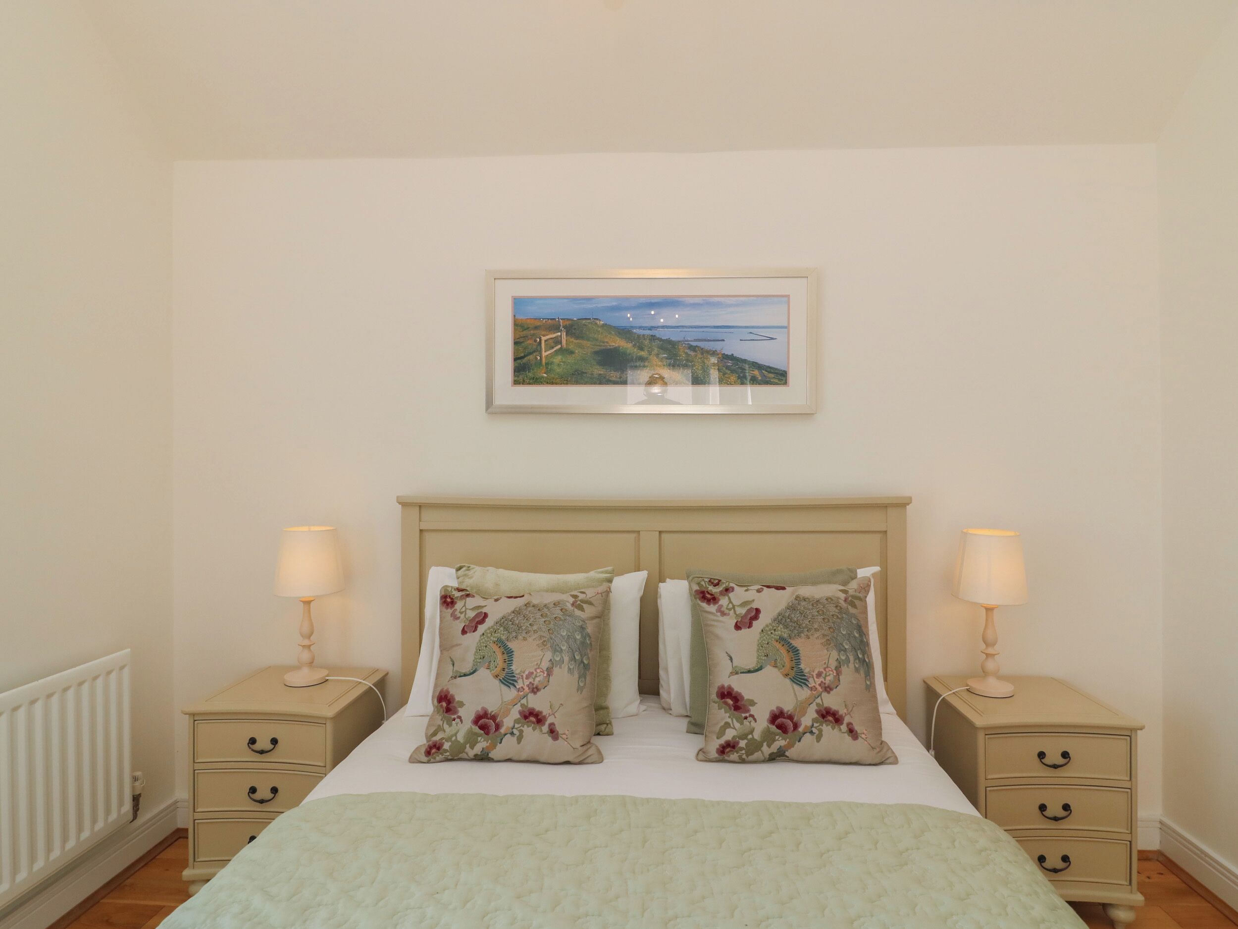 A bedroom with a bed, two nightstands, and a painting above the bed.