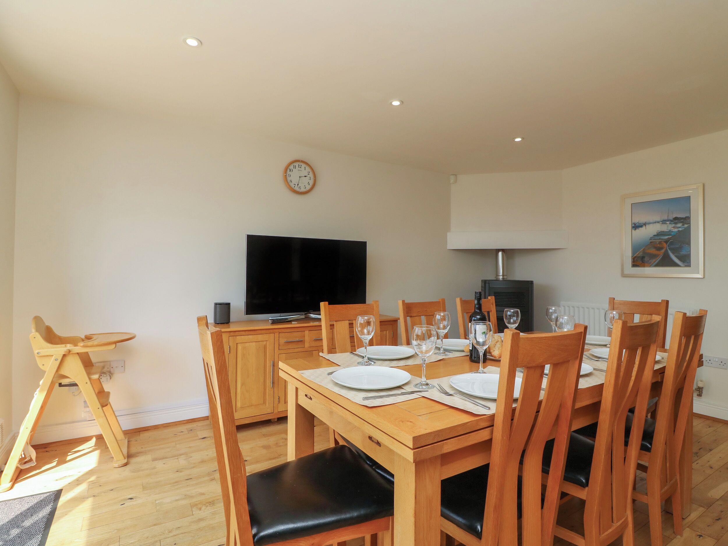 A dining area with a wooden table set for six, a television, and a fireplace.