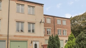 Un edificio residencial de dos plantas con fachada color beige, puerta verde y sección de ladrillo.