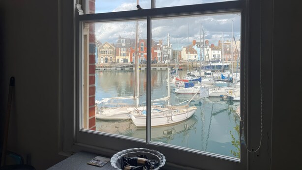 Une pièce dotée d’une grande fenêtre donnant sur une marina, avec des bateaux et des bâtiments.
