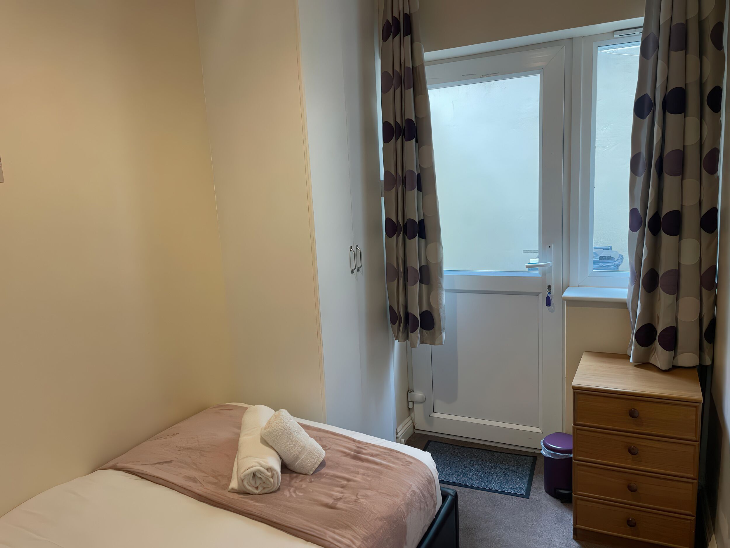 A bedroom with a bed, a dresser, a window with curtains, and a door.