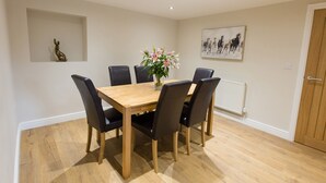 A dining area with a wooden table and black chairs, a vase with flowers, a wall-mounted artwork, and a radiator. - Minafon (Llangollen)