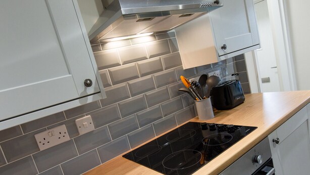 A modern kitchen with grey tiled backsplash, a black induction cooktop, and wooden countertops. - Minafon (Llangollen)