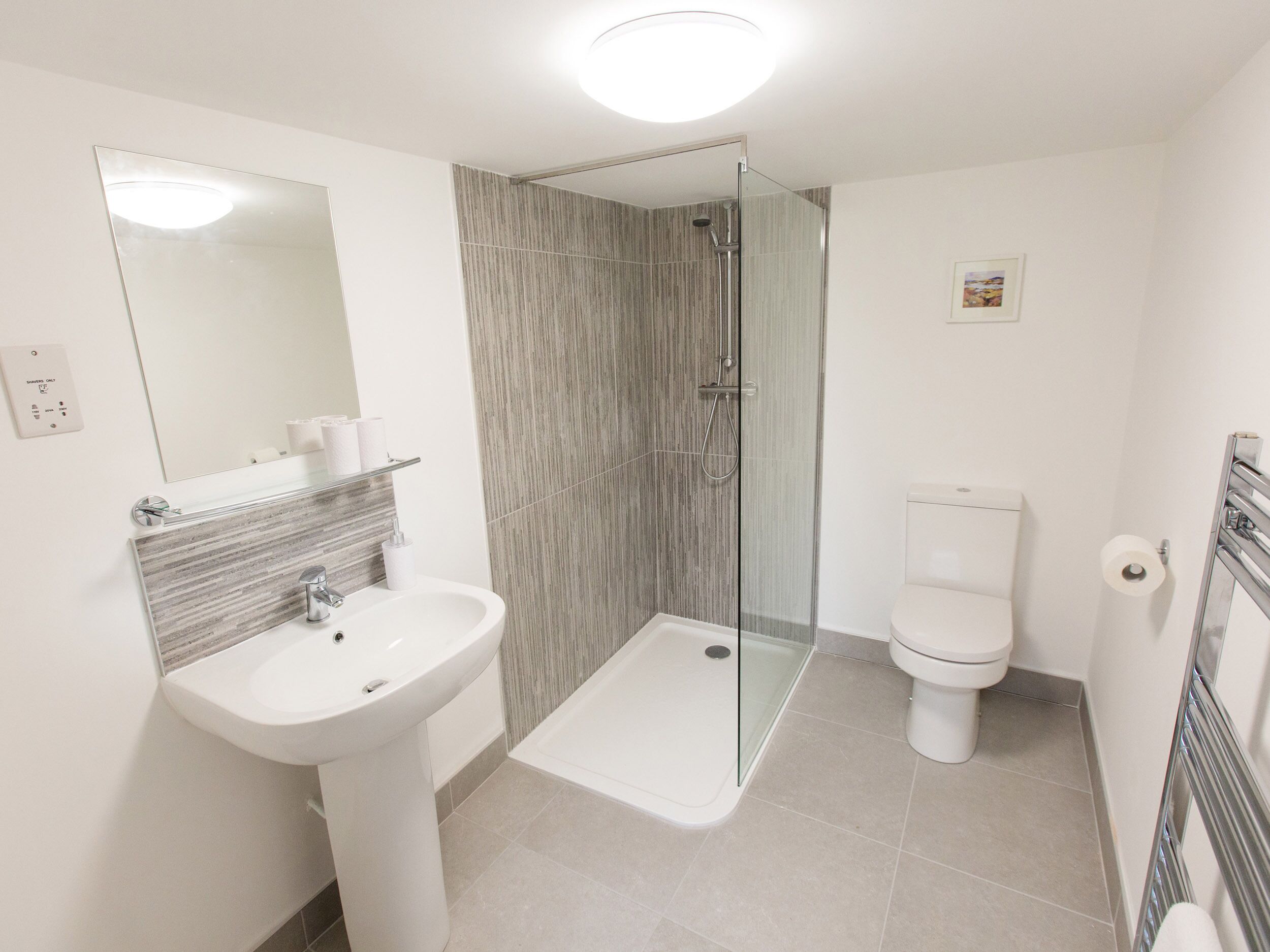 Un baño moderno con ducha envuelta en cristal, un lavabo blanco y un inodoro.