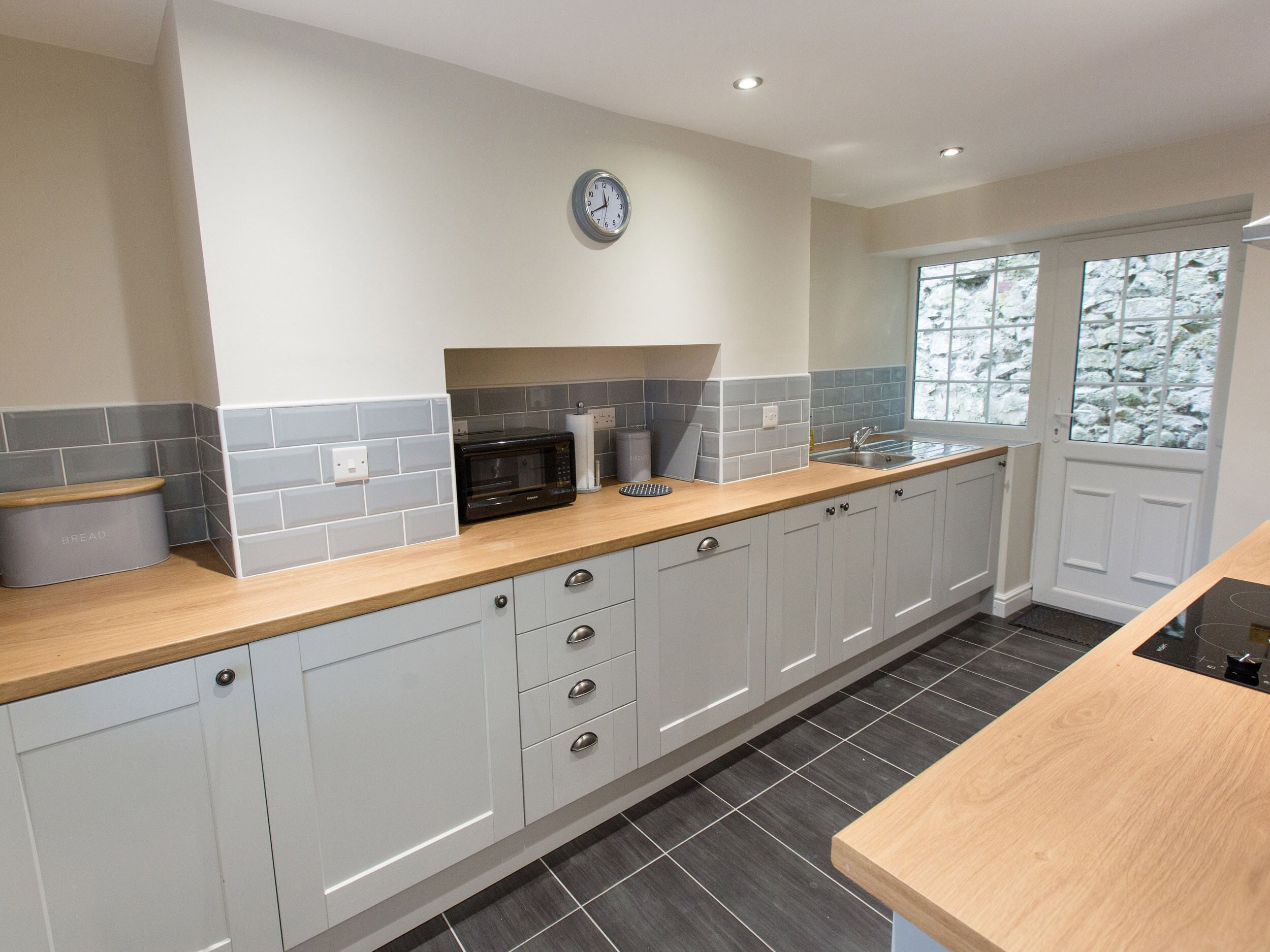 A modern kitchen with grey tiles, wooden countertops, and white cabinets.