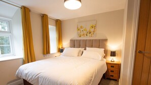 A neatly made bed in a hotel room with a window, a bedside table with a lamp, and a door. - Minafon (Llangollen)