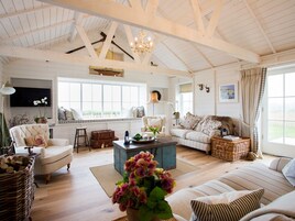 Amplia sala de estar con techo alto, vigas de madera, un ventanal grande, chimenea y televisor.