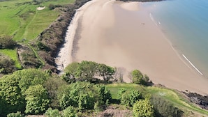 A coastal landscape with a sandy beach, green fields, and a body of water. - Lligwy Beach Cottage (Dulas)