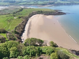 Paisaje costero con una playa arenosa, campos verdes y una masa de agua.