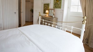 A bedroom with a white bed, a dresser with a mirror, and a painting on the wall. - Lligwy Beach Cottage (Dulas)