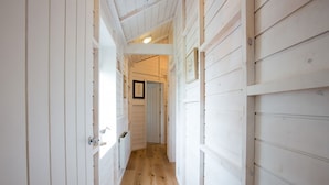 A narrow hallway with wooden walls and a wooden floor, leading to a door at the end. - Lligwy Beach Cottage (Dulas)