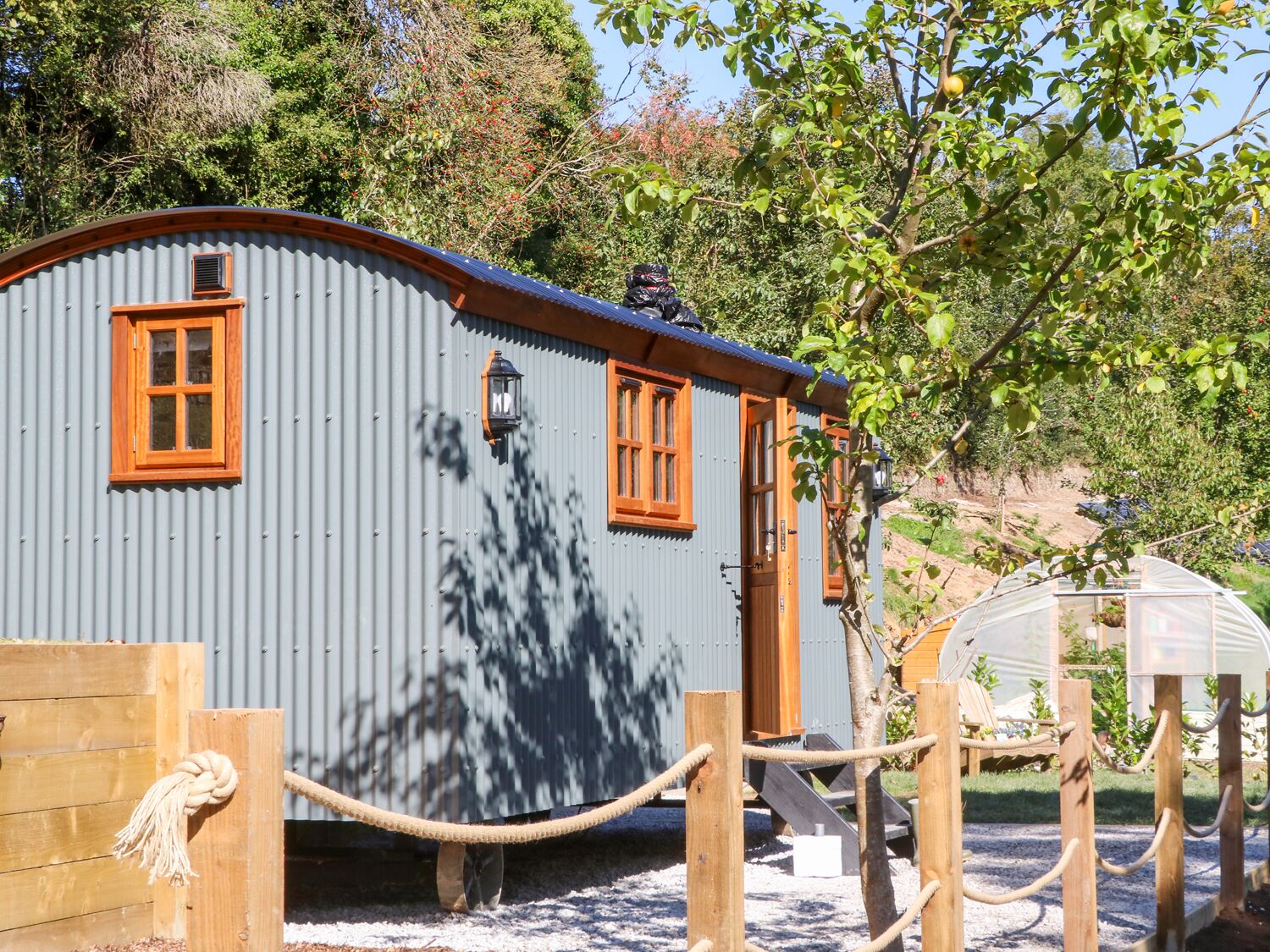 A small, rustic cabin with two windows and a door, surrounded by a rope fence and trees.