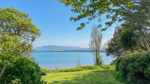 A grassy area with a view of a calm body of water and distant hills. - Reaver (Weymouth)