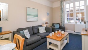 A cozy living room with a grey sofa, a wooden coffee table, and a dining area with a white table and chairs. - Reaver (Weymouth)
