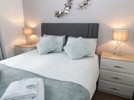 A neatly made bed with striped bedding and fluffy pillows, two bedside tables with lamps, and a wall-mounted decorative piece.