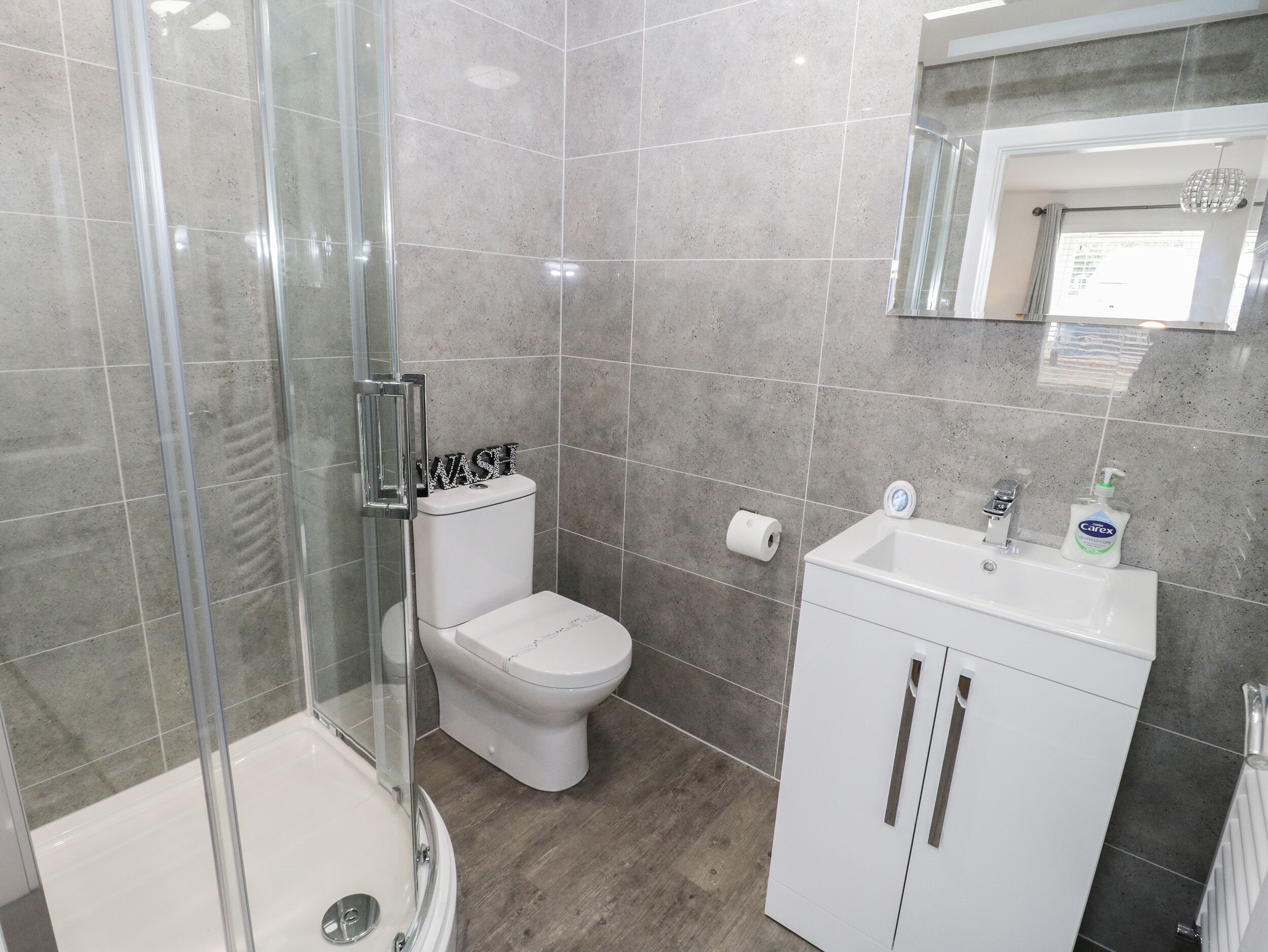Un bagno moderno con box doccia in vetro, un water e un lavandino con dispenser di sapone.