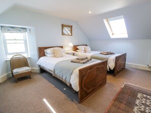 A bedroom with two wooden beds, a rattan chair, a small table with a lamp, and a window providing natural light. - Marl House (Newton Stewart)