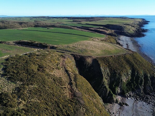 Un paisaje costero con campos verdes, un acantilado y una playa.