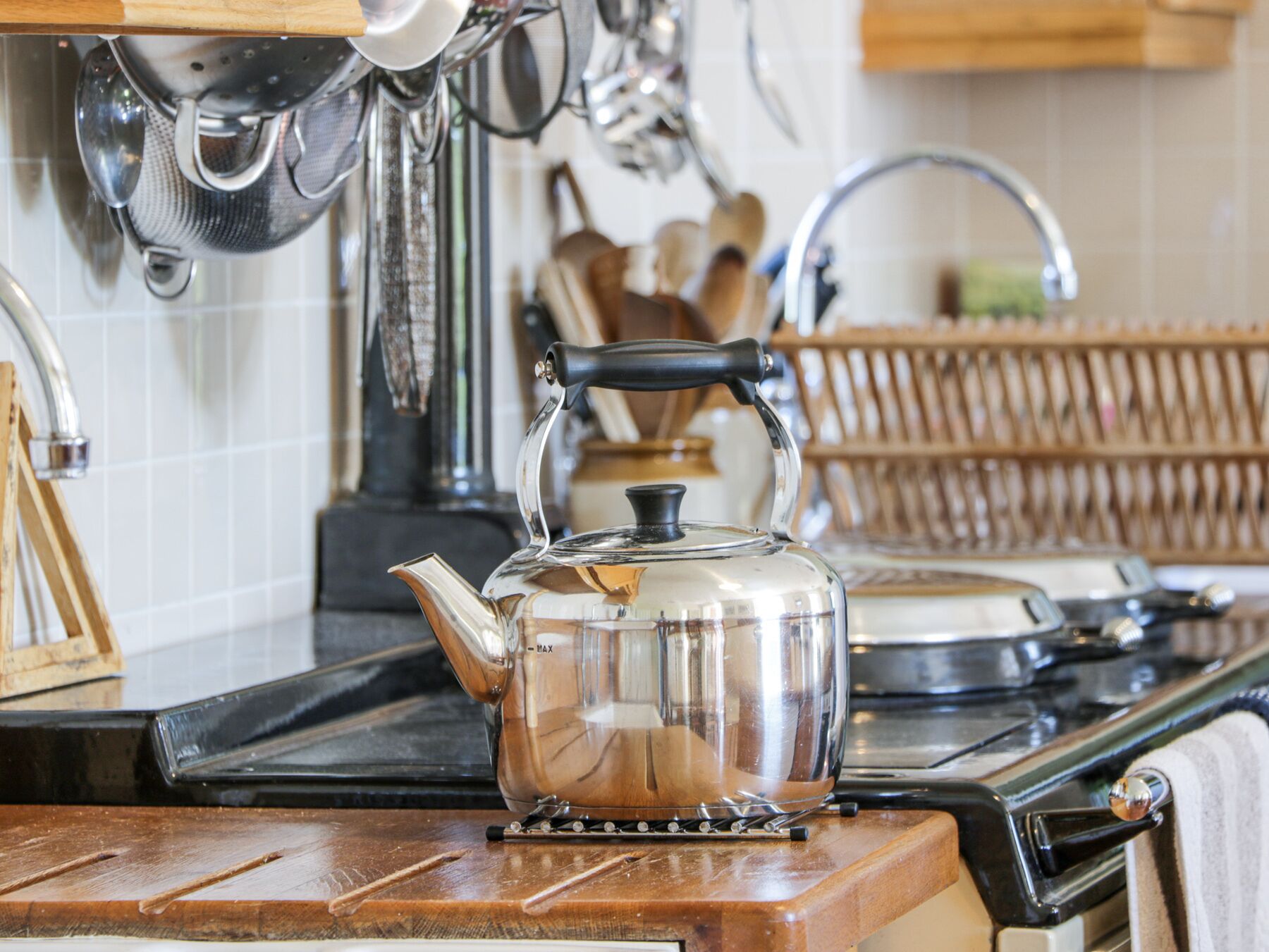 Une cuisine avec une bouilloire en acier inoxydable sur la cuisinière, une passoire suspendue au-dessus de l’évier et des ustensiles en bois rangés sur un présentoir.
