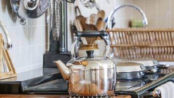 Une cuisine avec une bouilloire en acier inoxydable sur la cuisinière, une passoire suspendue au-dessus de l’évier et des ustensiles en bois rangés sur un présentoir.