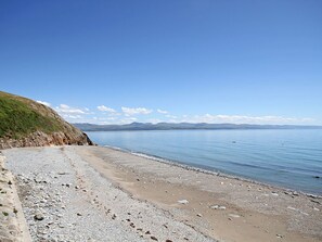 A beach with a pebbly shore and a clear view of the water and distant mountains. - Mor Edrin (Criccieth)