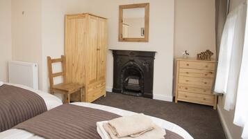 A bedroom with a bed, a wooden wardrobe, a dresser, a fireplace, and a mirror.
