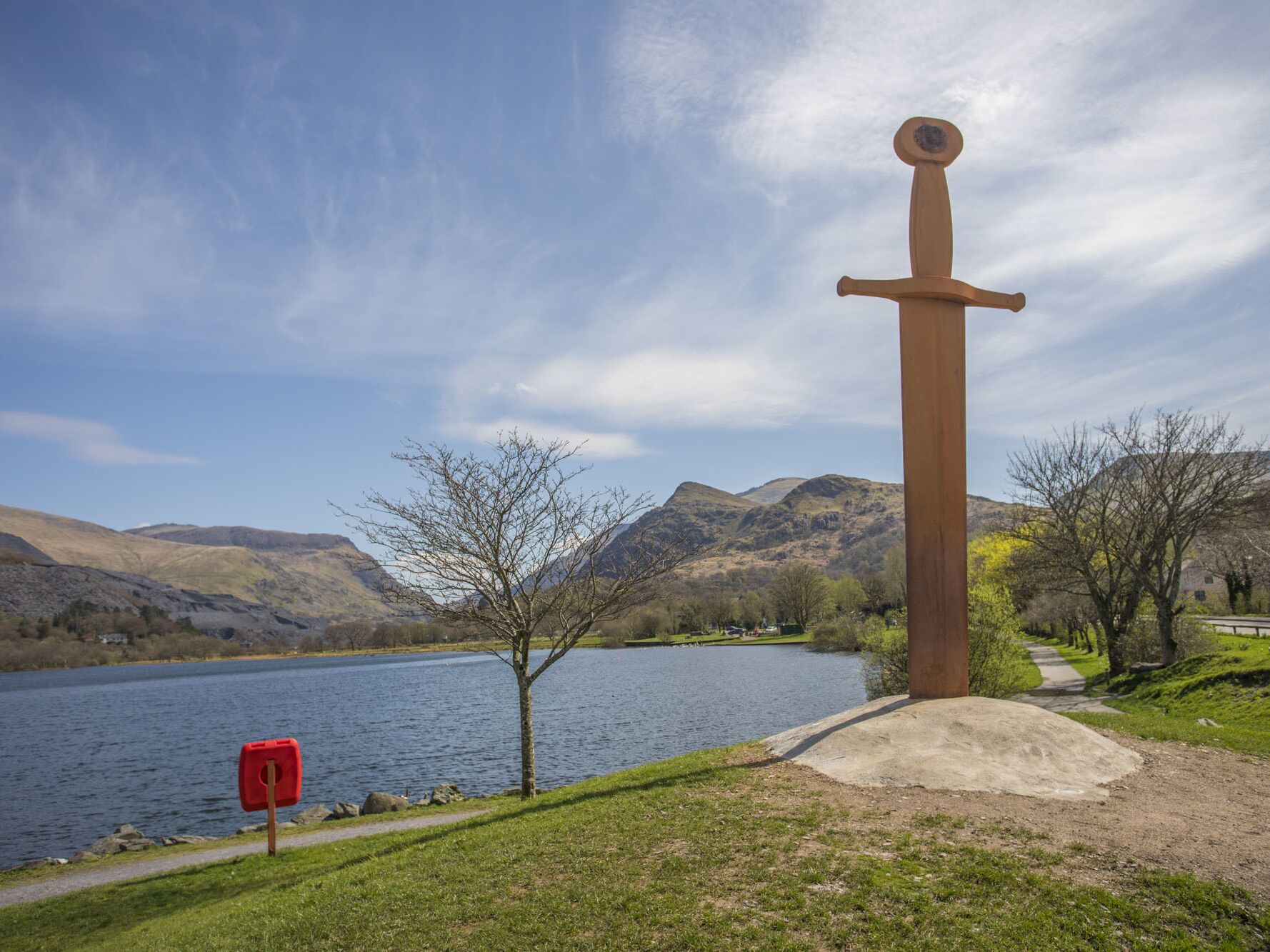 A sword monument by a lake with mountains in the background.