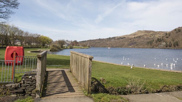 A wooden pathway leading to a lake with ducks and a boat in the distance. - Hirfron (Caernarfon)