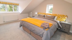 A bedroom with a sloped ceiling, a bed with a yellow throw, a nightstand, and a window with a view of greenery. - Runswick (York)