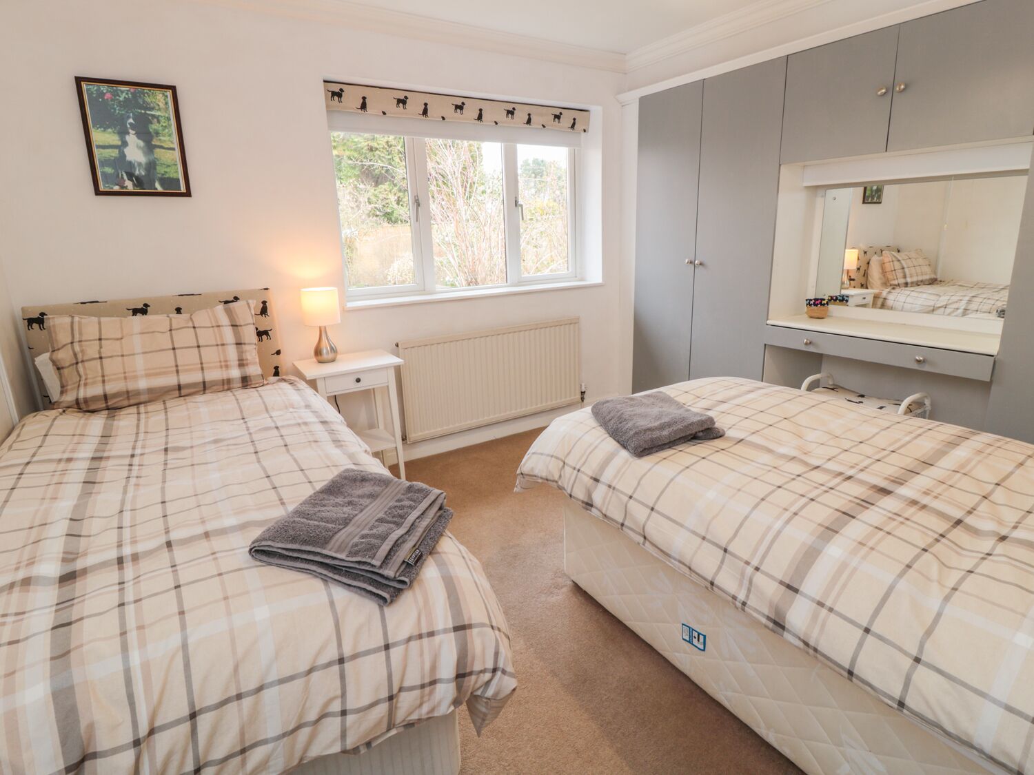 A bedroom with two beds, a window with a view, a bedside table with a lamp, and a wardrobe.