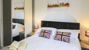 A hotel room with a bed, a mirror, a cityscape painting, and two bedside lamps.