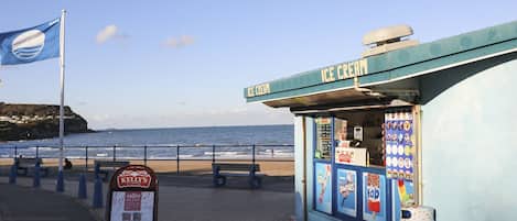 A beachside ice cream cart with a sign reading "ICE CREAM" and a nearby sign for "KELLY'S".