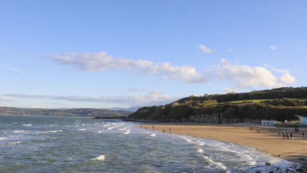 A beach with waves, people, and a hilly landscape in the background.