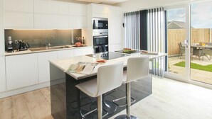 A modern kitchen with white cabinetry, a central island with bar stools, and a dining area with a table and chairs.
