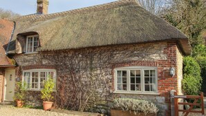 A traditional brick house with a thatched roof, two windows, and a chimney. - Little Forge (Wareham)