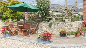 An outdoor patio with a stone wall, wooden furniture, and potted plants. - Little Forge (Wareham)