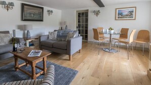 A modern living room with a grey sofa, a wooden coffee table, and a dining area with a glass table and metal chairs. - Little Forge (Wareham)