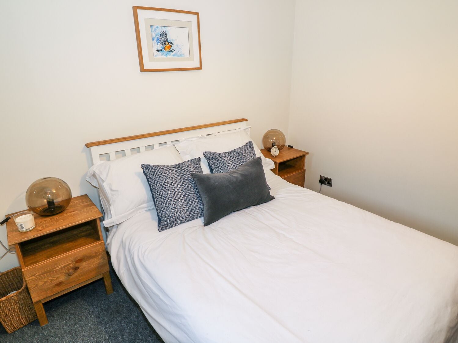 A neatly made bed with white bedding and two pillows, a wooden headboard, two bedside tables with lamps, and a framed picture on the wall.