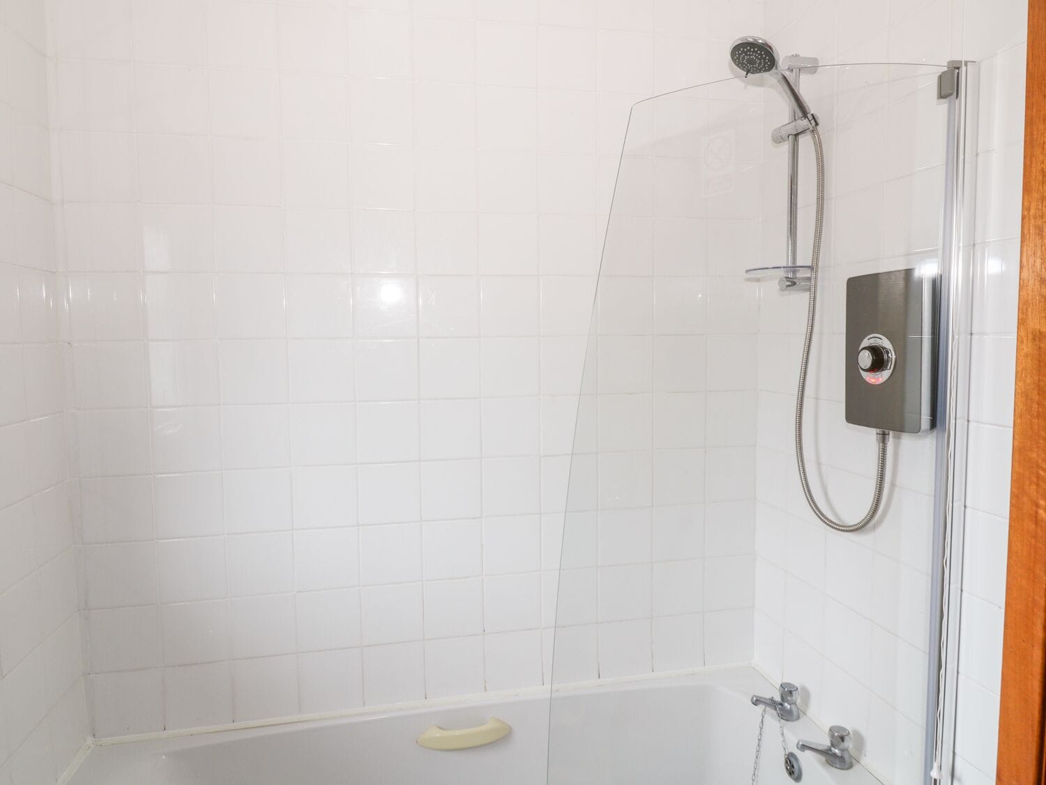 A modern bathroom with white tiled walls, a glass shower enclosure, and a bathtub with a handheld showerhead.