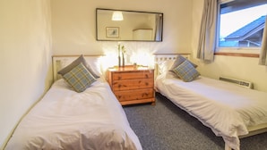 Une chambre avec deux lits simples, une commode en bois, un miroir et une fenêtre avec des rideaux.