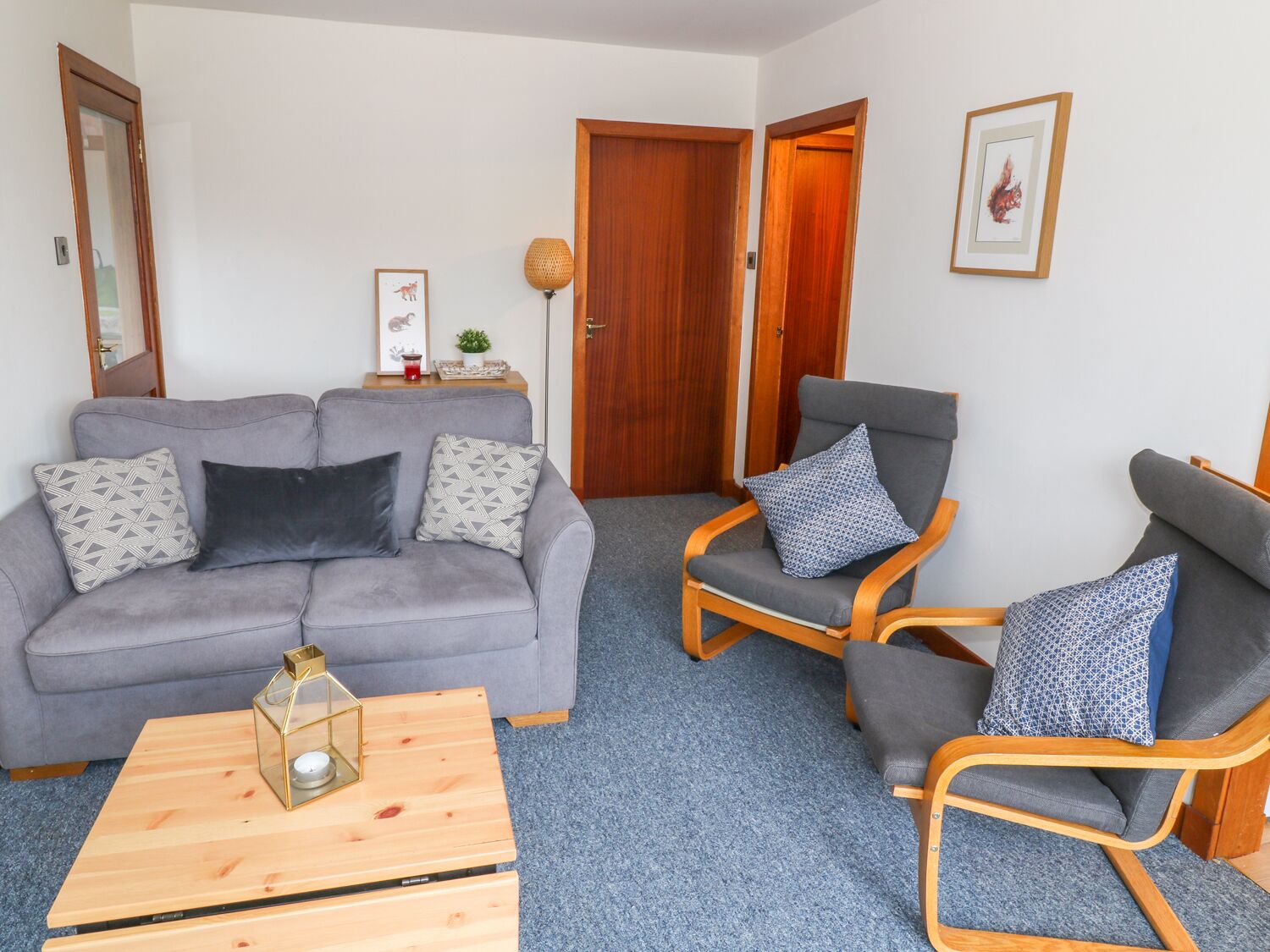 A living room with a grey sofa, two wooden chairs, a coffee table, and a door leading to another room.