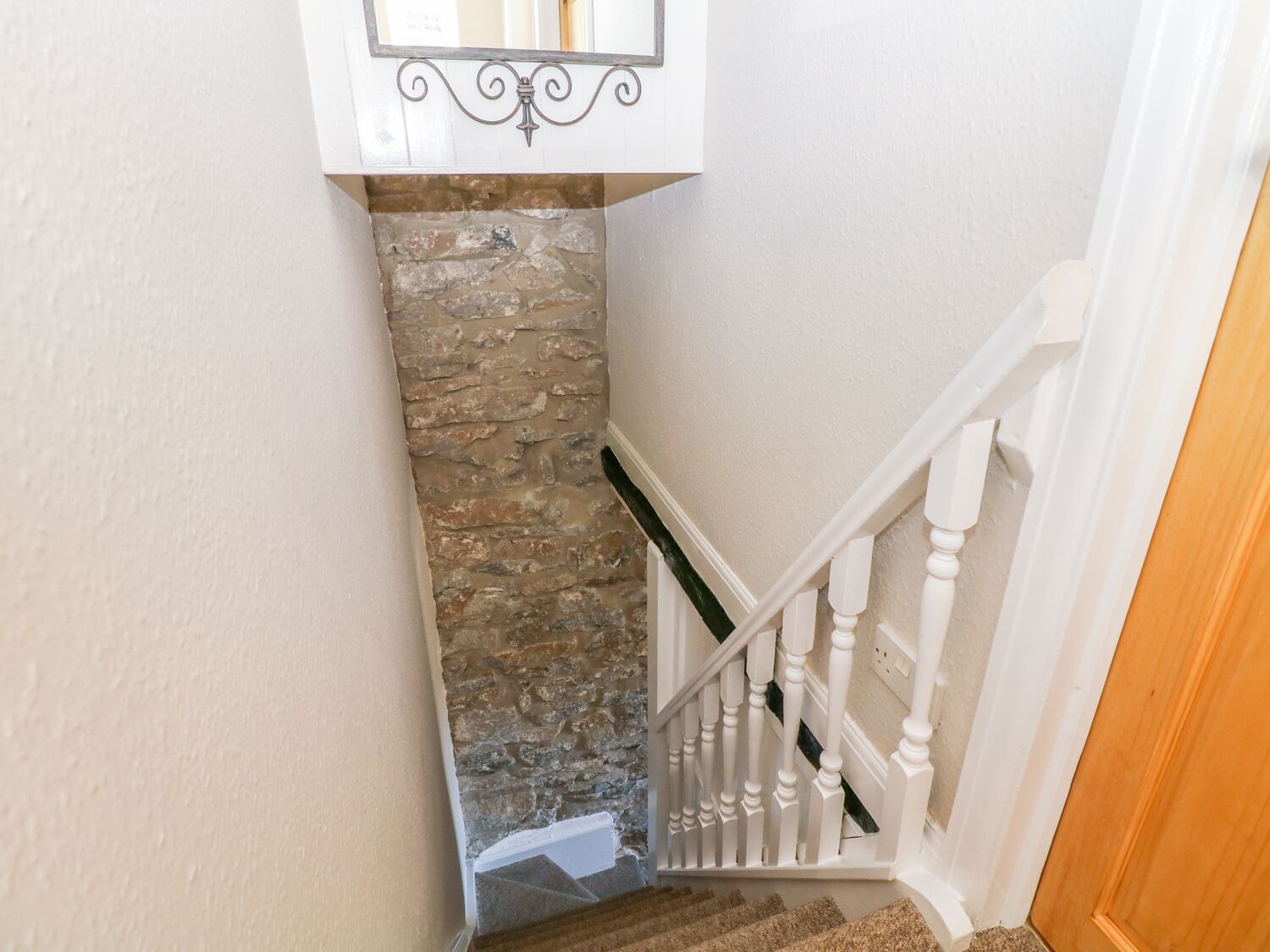 A staircase with a stone wall, white railing, and a wooden door at the bottom.