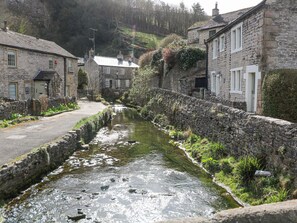 A narrow stone-lined water channel in a rural village with stone buildings on either side. - High View Cottage (Hope Valley)